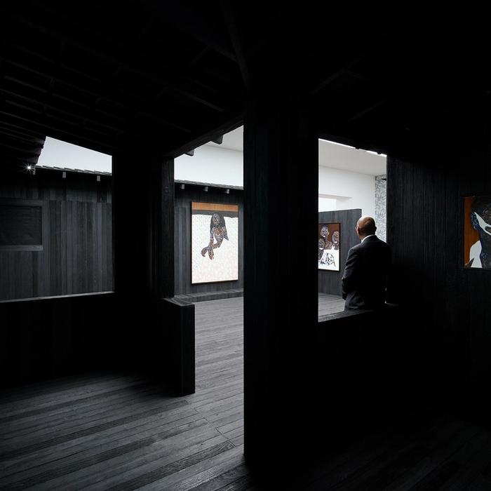 A digital render of a wall with print on it next to a wall with text on it. Two people stand next to these walls, while a third is framed by the entrance into a further room on the horizon.