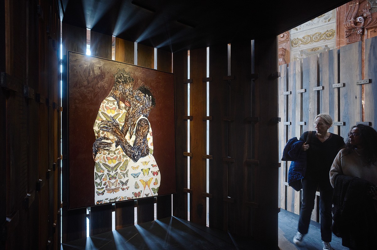 A figure on the right of ther photo looks at a painting hanging on panels with space in between them