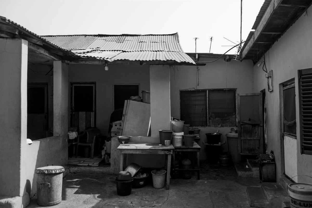 A black and white photograph of the courtyard to a building, surrounded by doors, walls, and roofing.