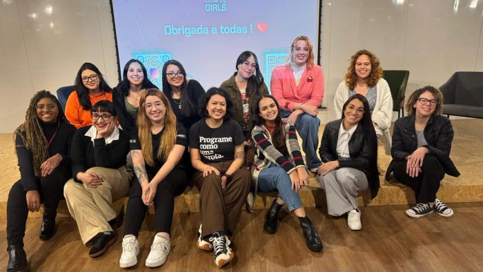 Embaixadoras universitárias da WoMakersCode juntas em evento presencial, algumas estão sentadas, e outras em pé