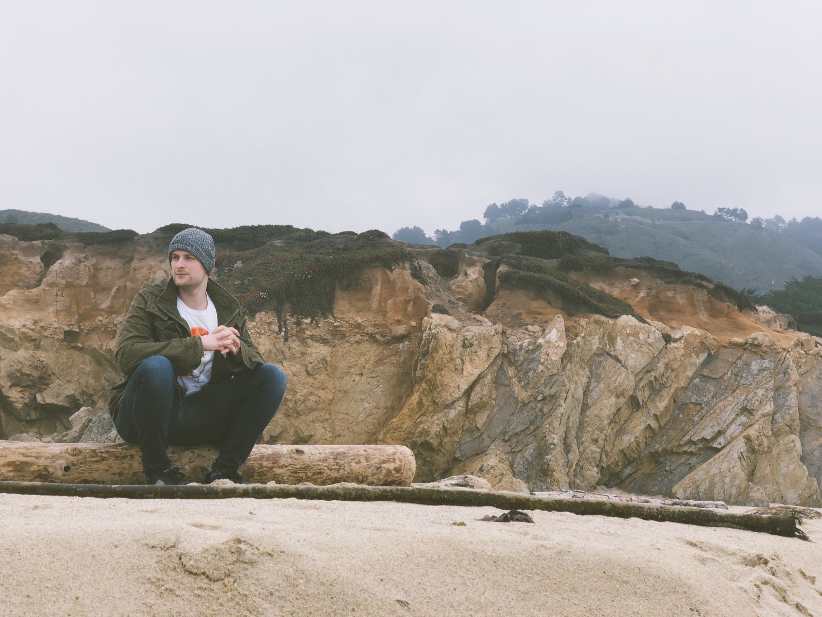 A man sitting on a log in front of hills