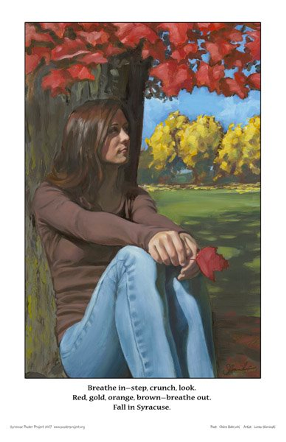 A woman sits under a tree in autumn holding a leaf