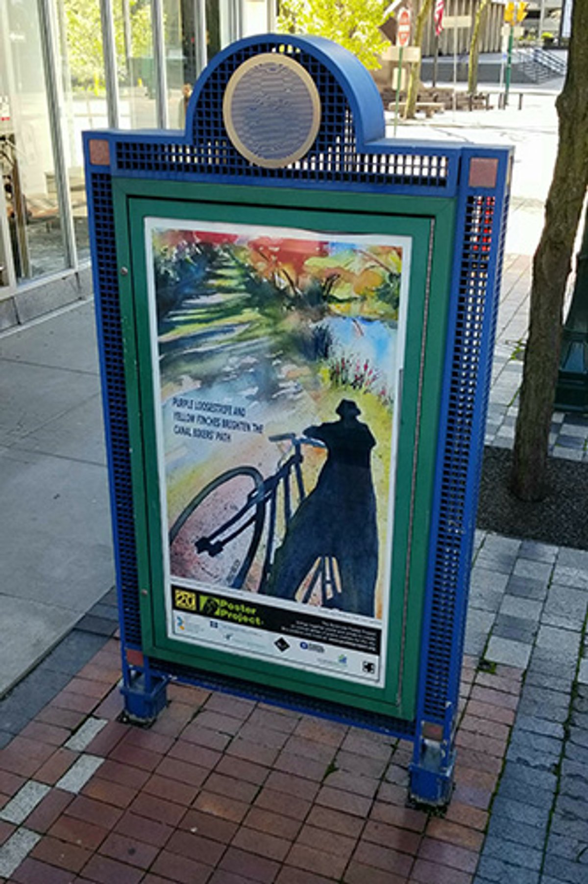 A kiosk with a poster of a person and a bicycle cast in shadow