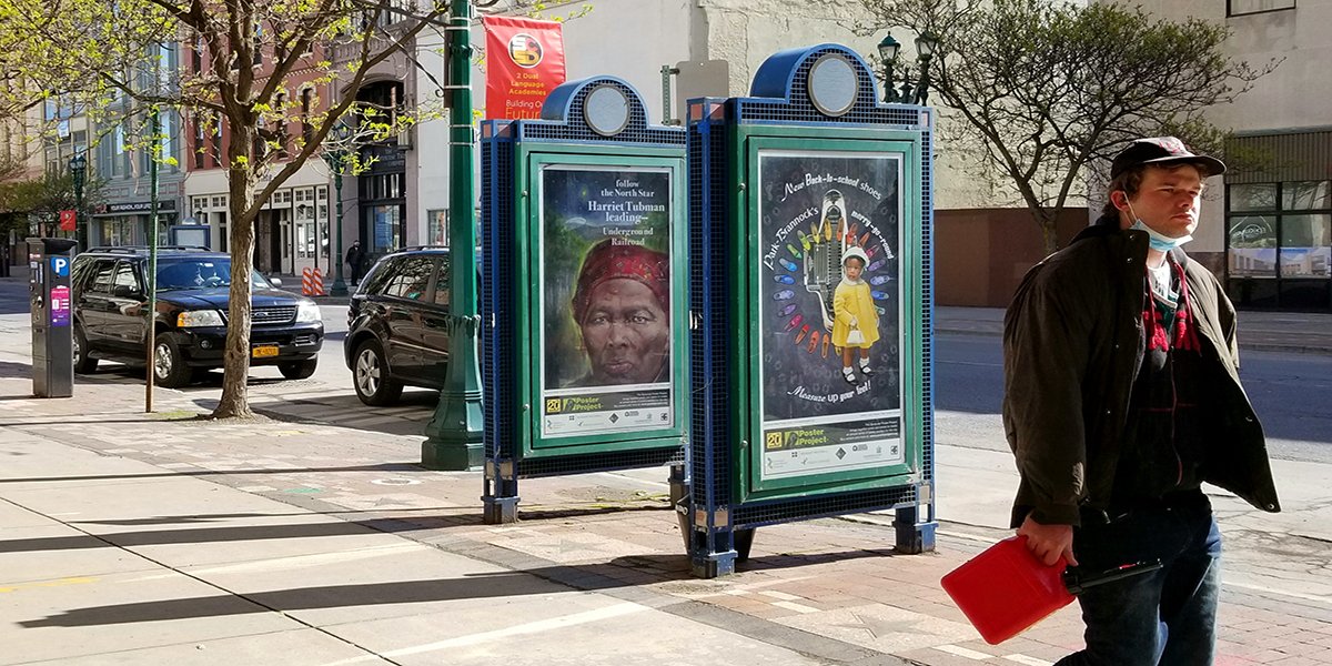 A man walking by two kiosks in Syracuse, NY