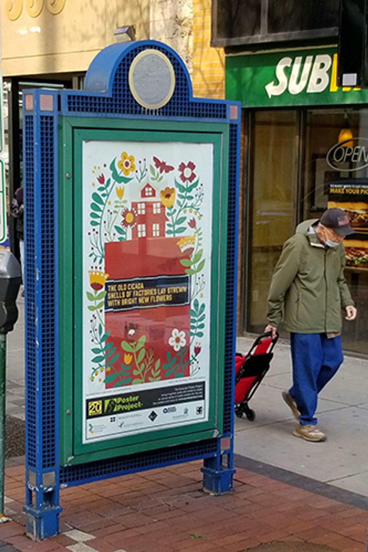 A person walking past a colorful kiosk with a poster of flowers