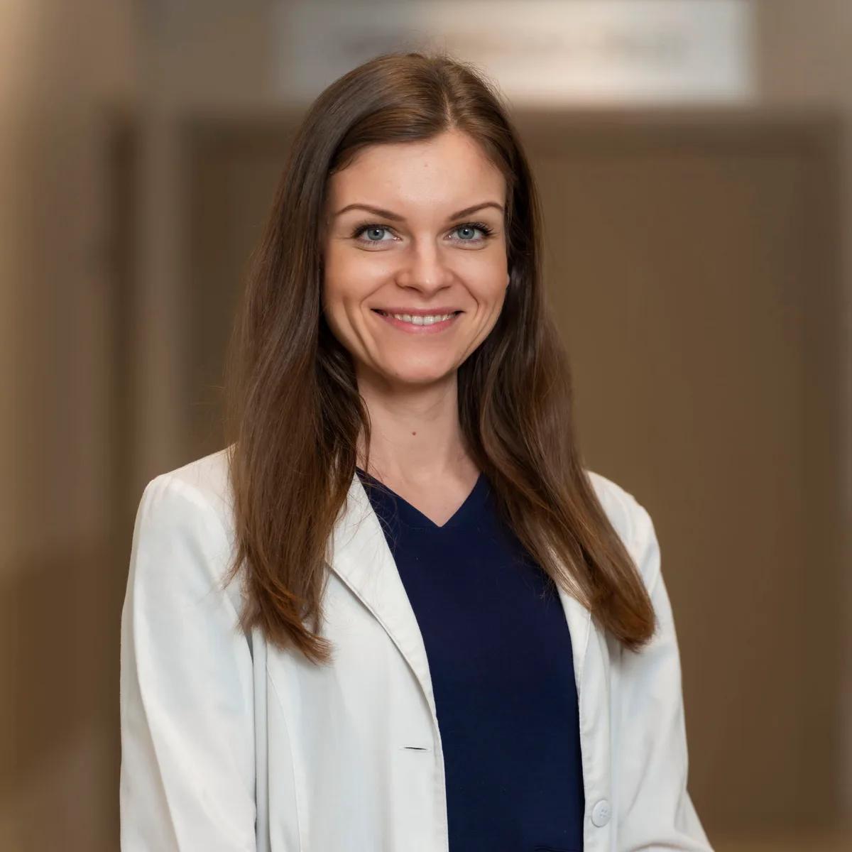 Professional headshot of a woman in a white coat with a softly blurred office background