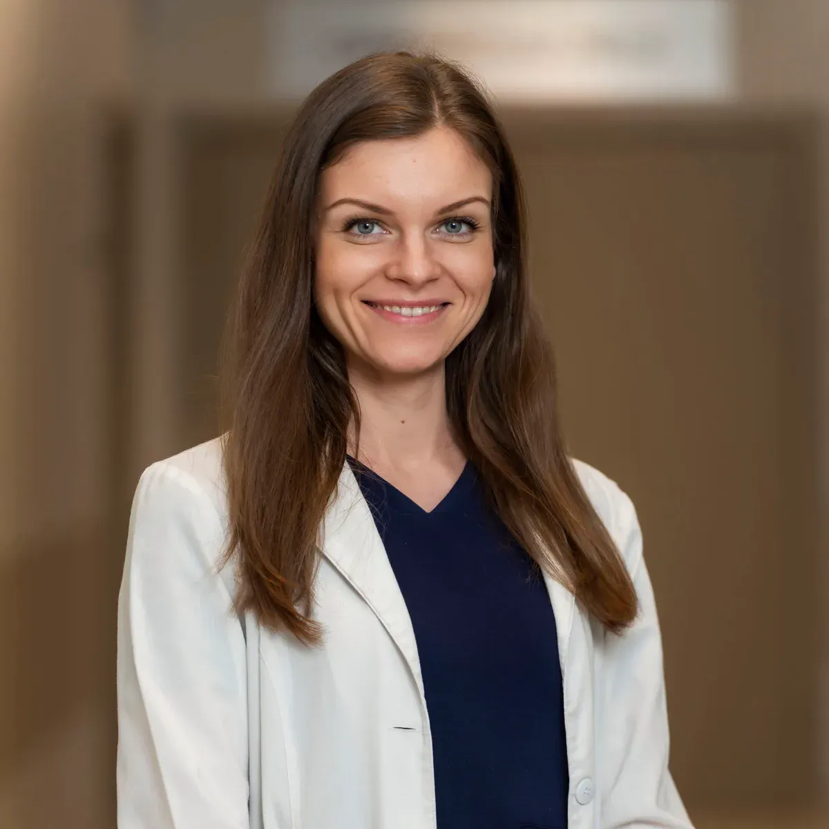 Professional headshot of a woman in a white coat with a softly blurred office background