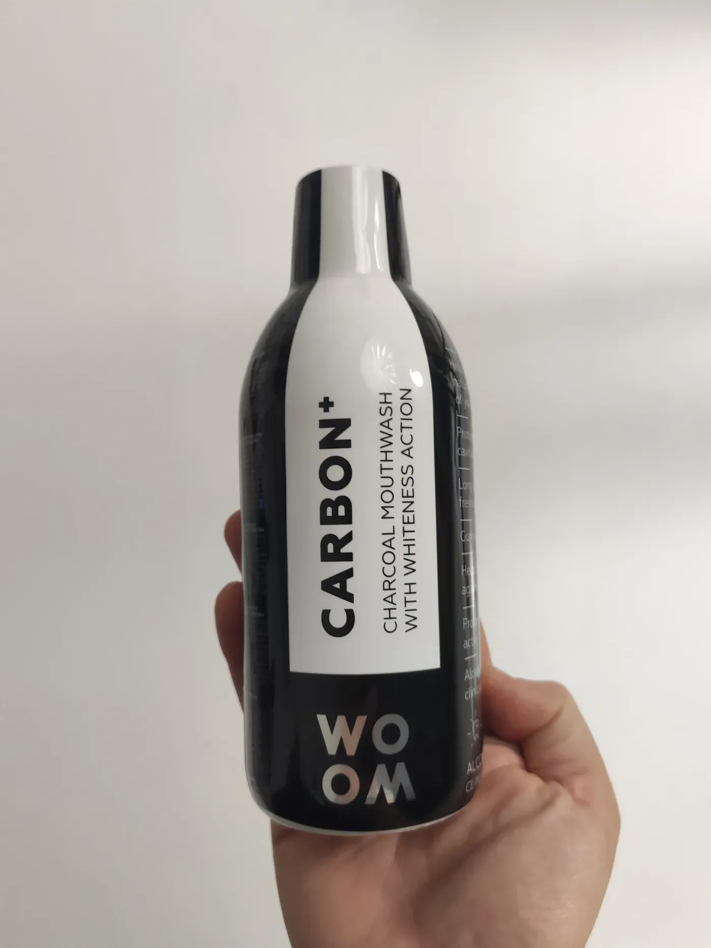 Original photo of a Woom Carbon+ charcoal mouthwash bottle held in a hand