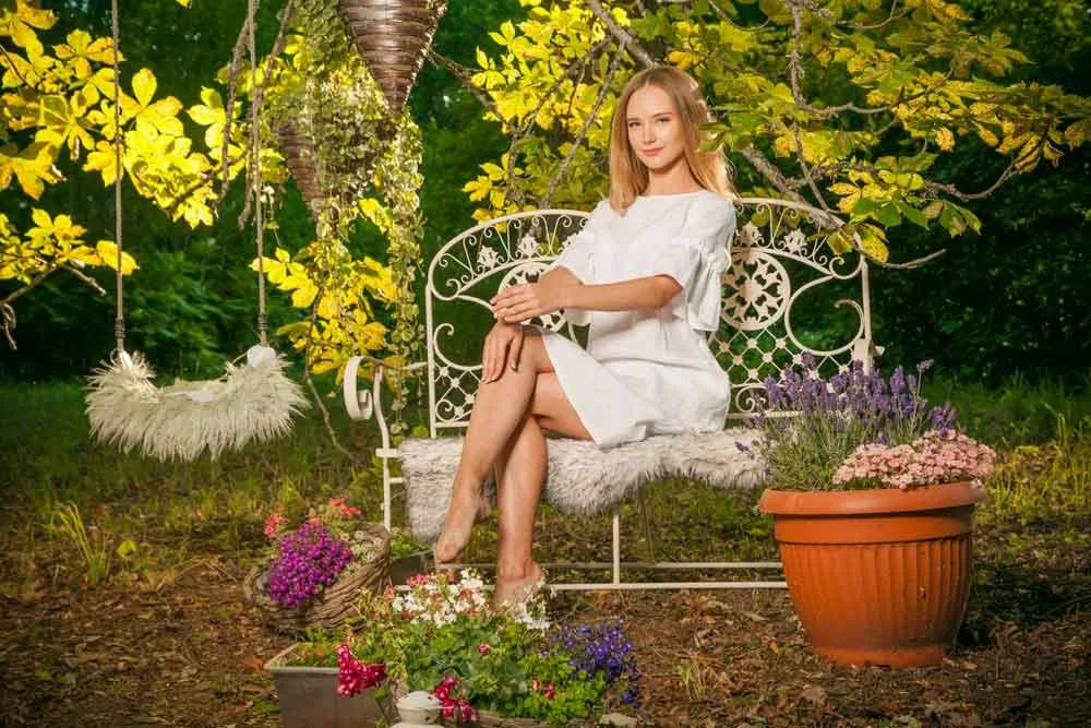 Model in a white dress sitting on a garden bench among flowers