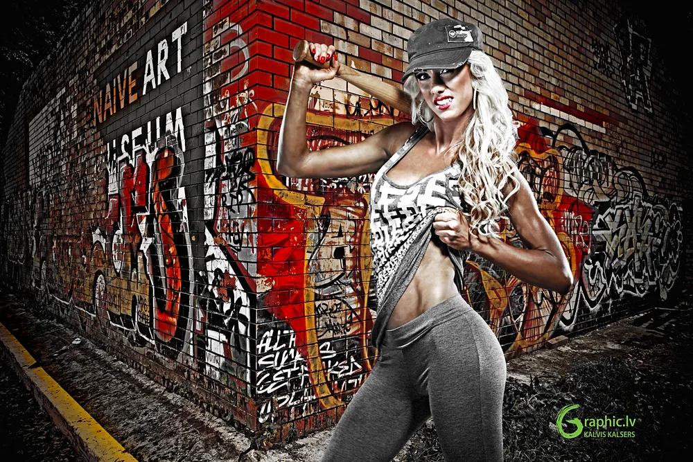 Fitness model in activewear posing with a baseball bat against a graffiti wall