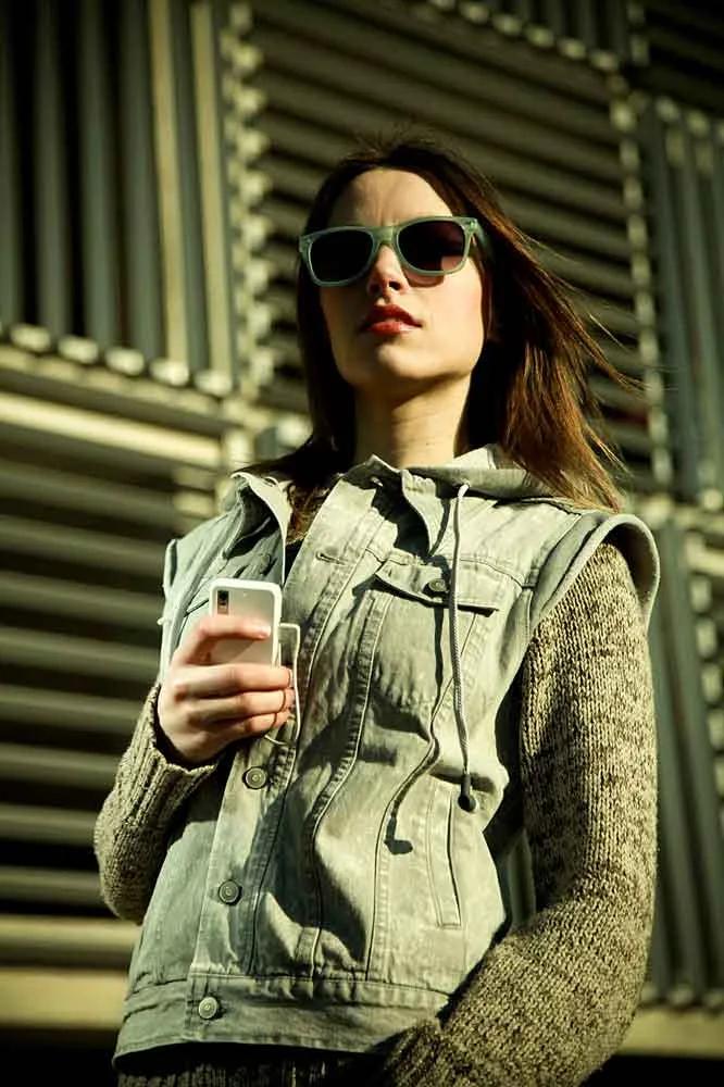 Model in a denim jacket wearing sunglasses against a striped metal wall