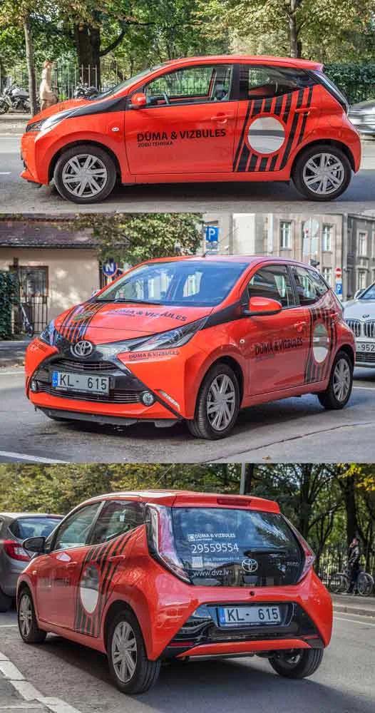 Oranžs un melns Toyota aplīmējums Dūma un Vizbules zīmolam, fotografēts no trim leņķiem pilsētas ielā