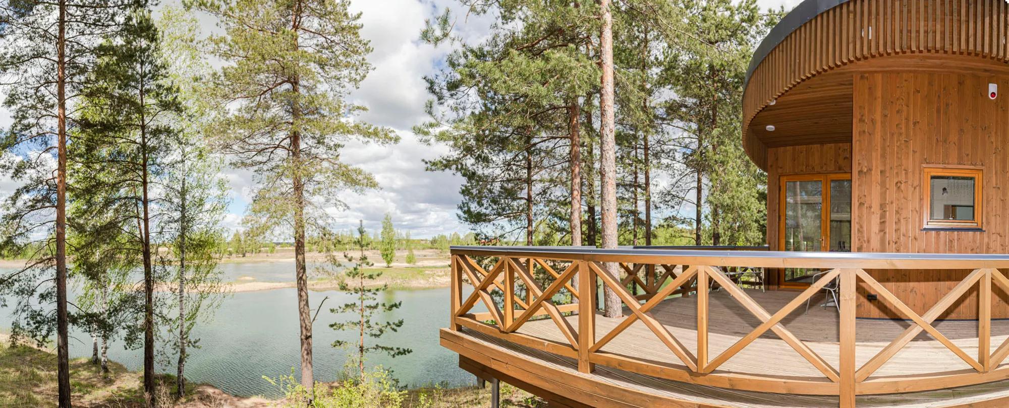 Panoramic photo of a round wooden lake house deck surrounded by pine and birch trees
