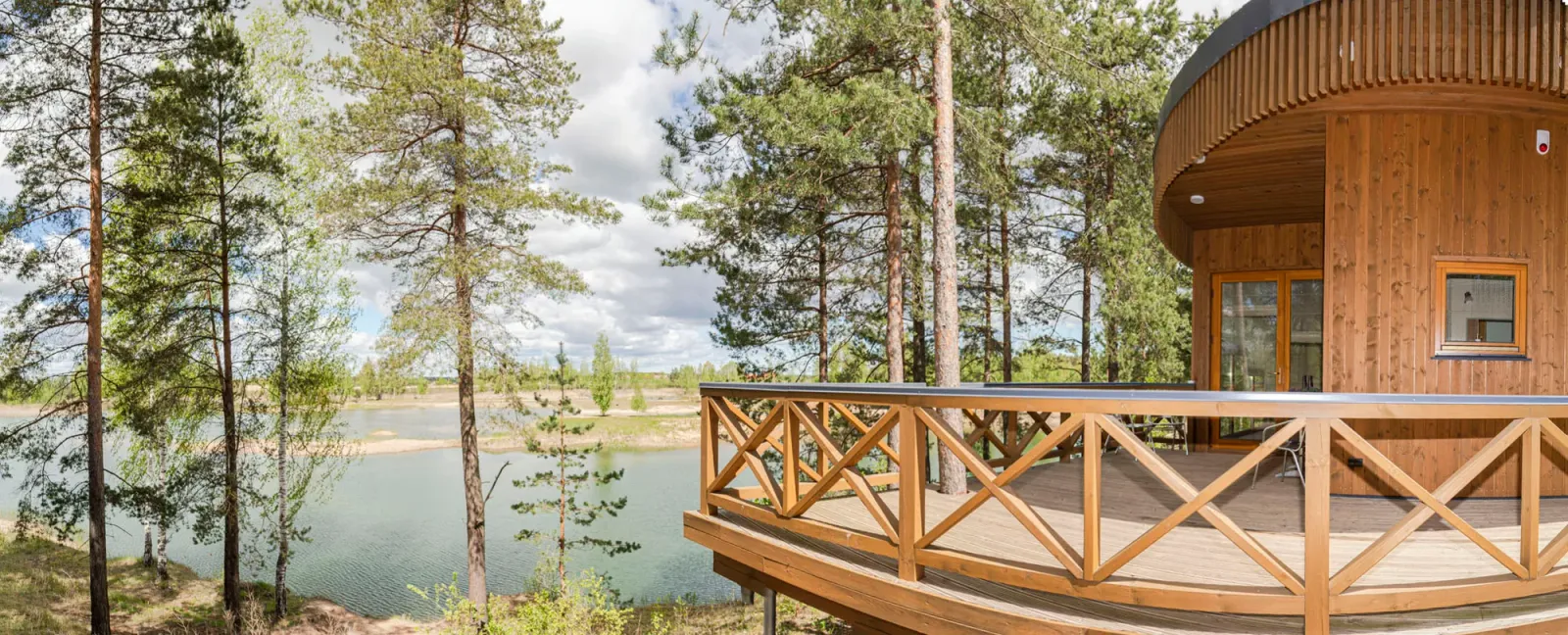 Panoramic photo of a round wooden lake house deck surrounded by pine and birch trees