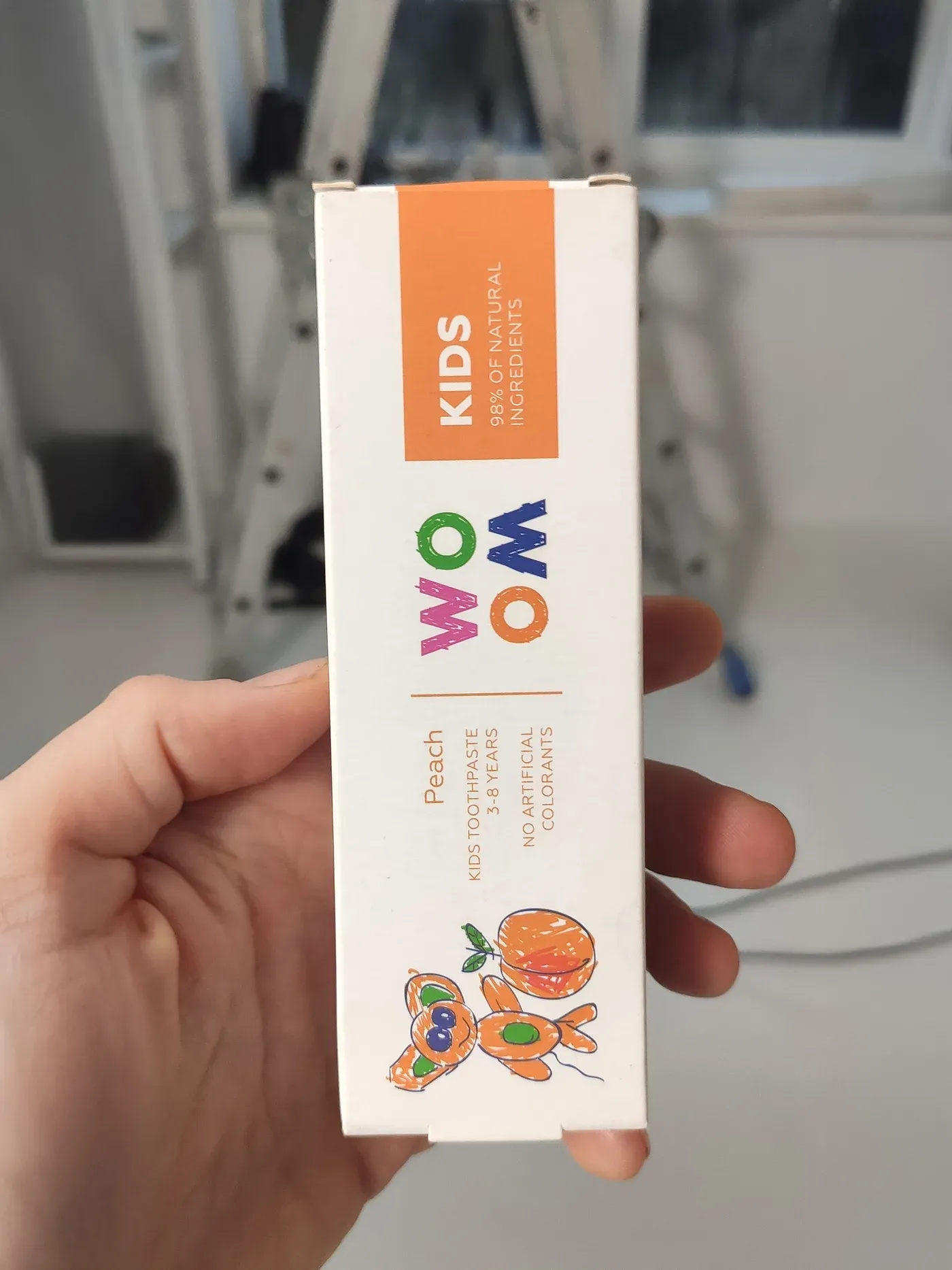 Original photo of a Woom Kids peach toothpaste box held in a hand