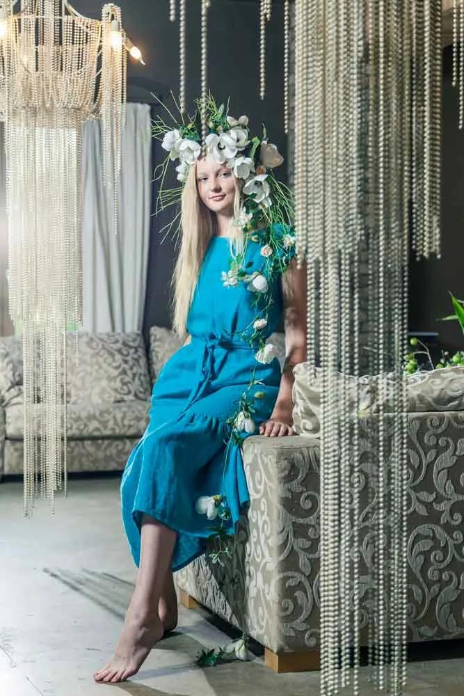 Model in a teal dress with a floral crown between hanging bead curtains
