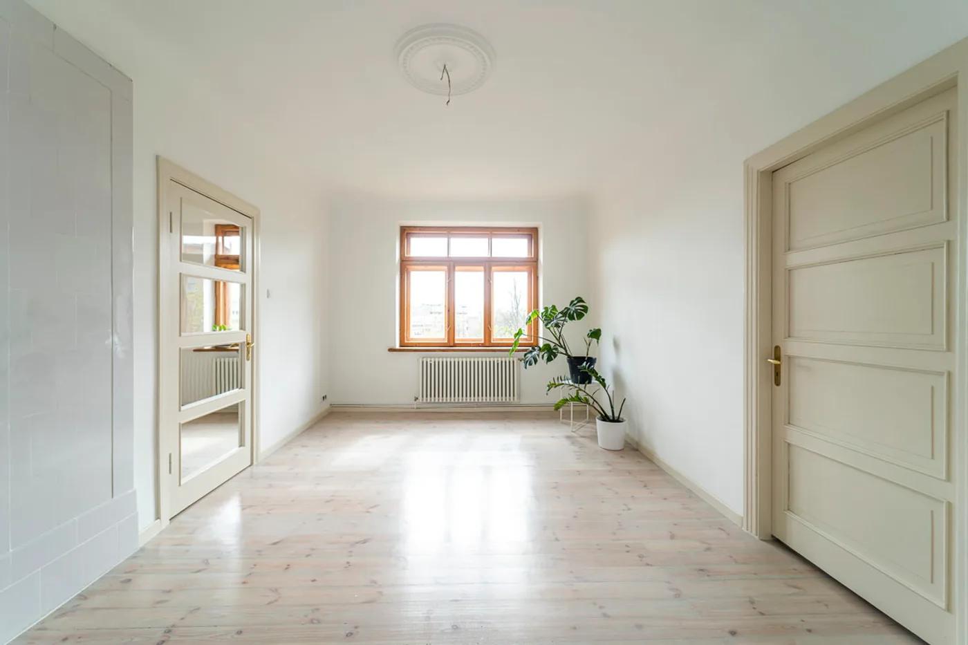 Bright empty apartment room with light wood flooring and a large window