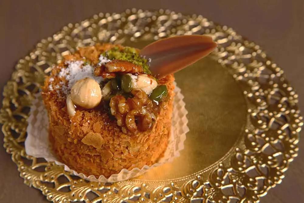 Plated dessert with caramelized nuts and pistachio on a gold charger plate