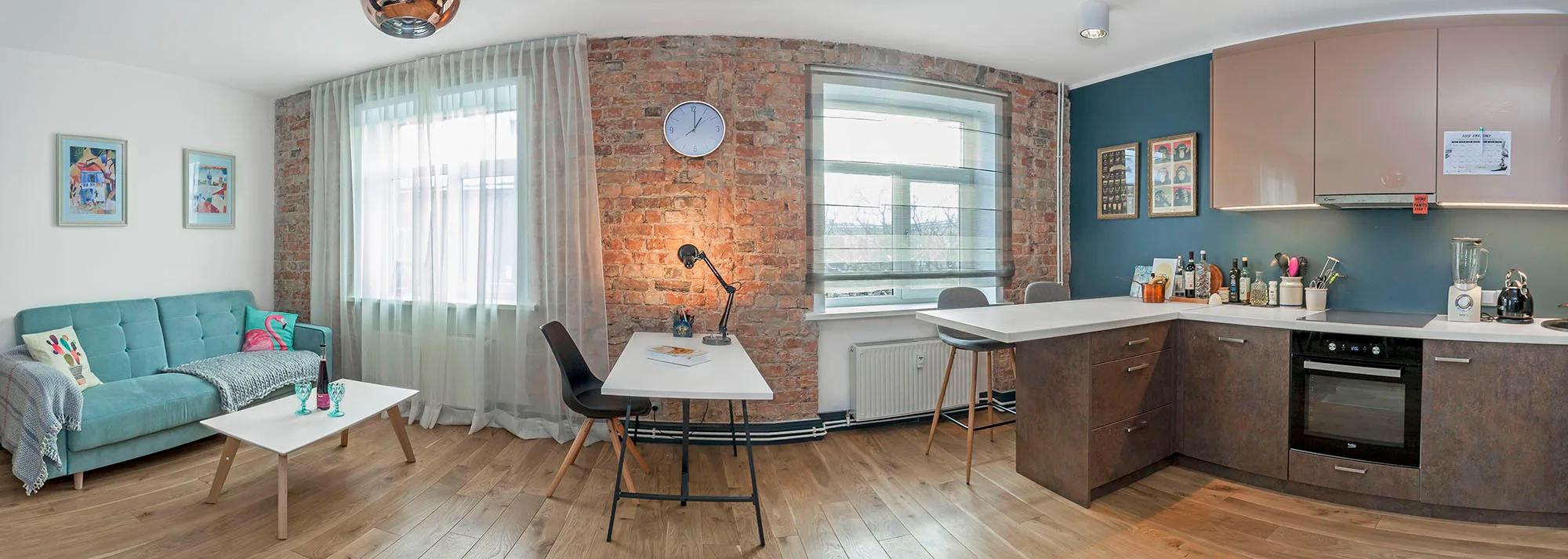 Panoramic photo of an open-plan living room and kitchen with an exposed brick wall