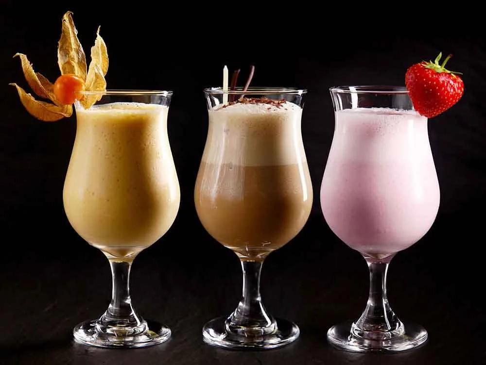 Three fruit milkshakes in glasses garnished with fruit