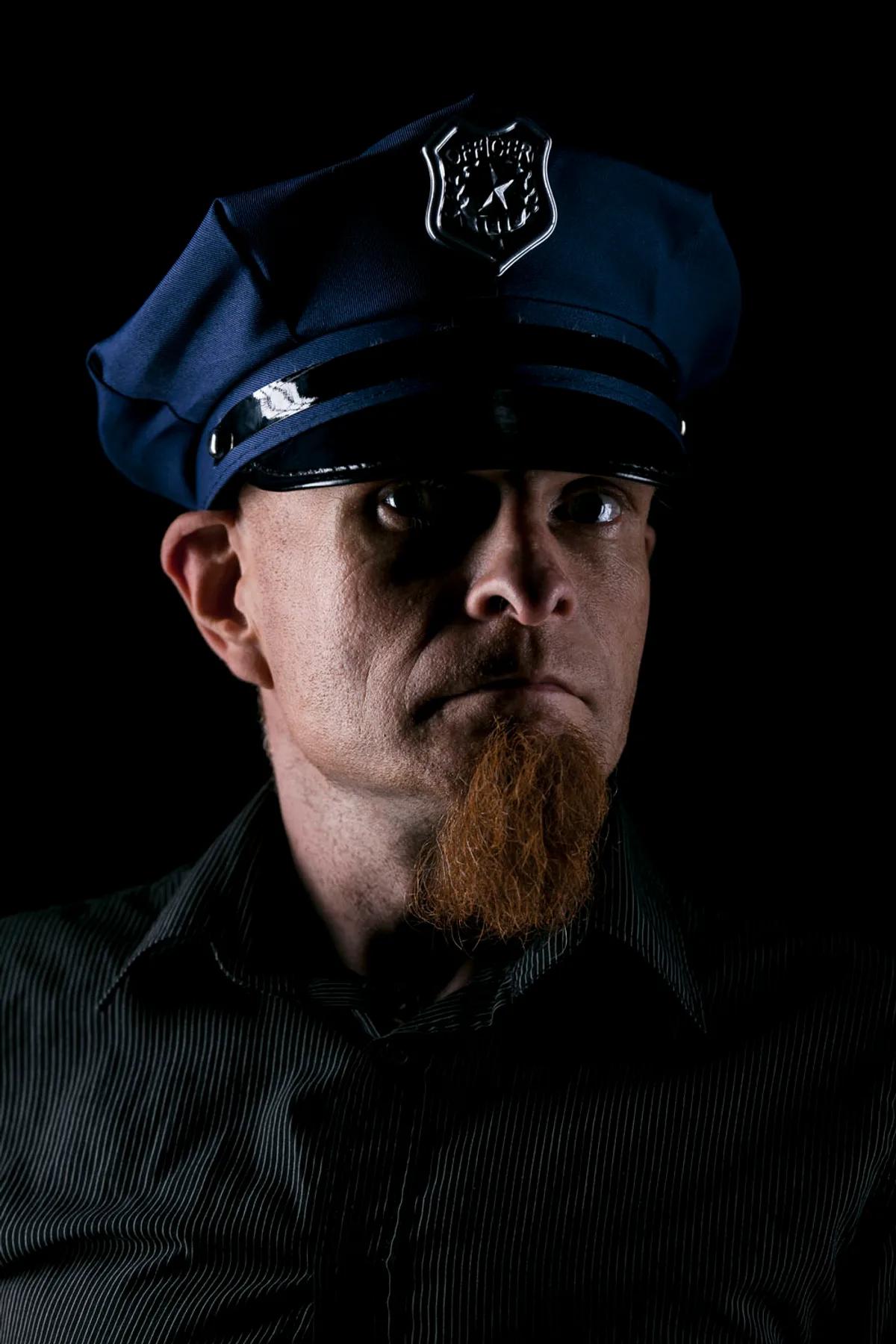 Editorial portrait of a man in a coat and helmet standing beside a motorcycle against a wooden wall