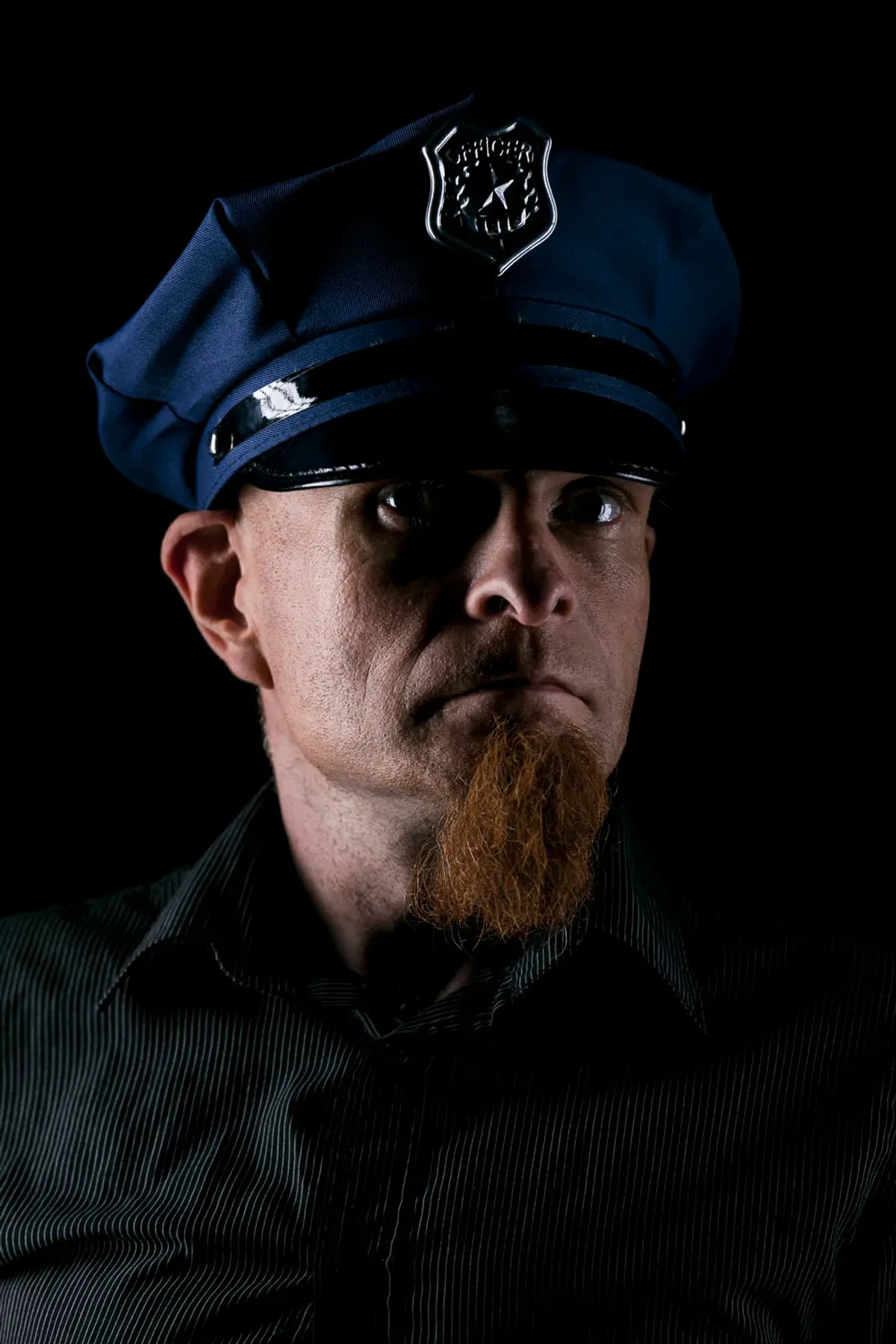 Editorial portrait of a man in a coat and helmet standing beside a motorcycle against a wooden wall