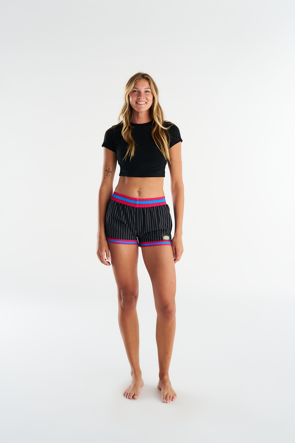 Woman wearing the Troy Field 2.0 customs, black boardshorts with white pinstripes and pink & blue waistband