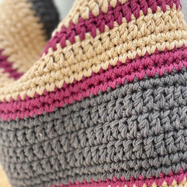 Primer plano detallado de una prenda tejida a mano con franjas de lana en colores gris, fucsia y beige, resaltando la textura y la calidad de los puntos artesanales de Nido Trama.