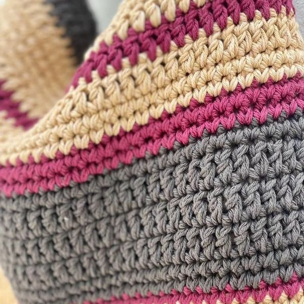 Primer plano detallado de una prenda tejida a mano con franjas de lana en colores gris, fucsia y beige, resaltando la textura y la calidad de los puntos artesanales de Nido Trama.
