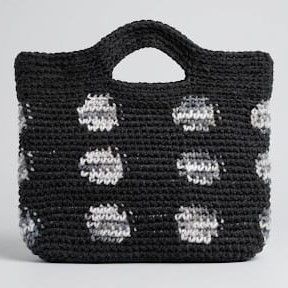 Bolso de mano de ganchillo negro de Nido Trama con patrón de lunares texturizados en blanco, gris y negro jaspeado, sobre un fondo gris claro.