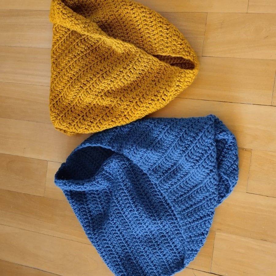 Vista superior de dos gorros de lana tejidos a mano, uno color mostaza y otro azul vibrante, apoyados sobre un piso de madera clara para resaltar la textura del crochet artesanal de Nido Trama.