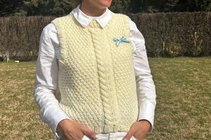 Primer plano de una mujer en un patio exterior vistiendo un suéter de la colección de otoño, destacando la textura del tejido artesanal y el diseño abrigado en un entorno natural.