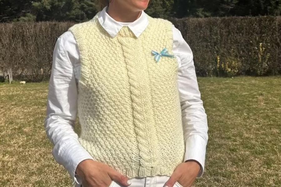 Primer plano de una mujer en un patio exterior vistiendo un suéter de la colección de otoño, destacando la textura del tejido artesanal y el diseño abrigado en un entorno natural.