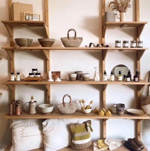 Estantería de madera clara con productos de Nido Trama: cestas tejidas, cuencos de cerámica, velas aromáticas y textiles para el hogar en tonos neutros y terrosos.