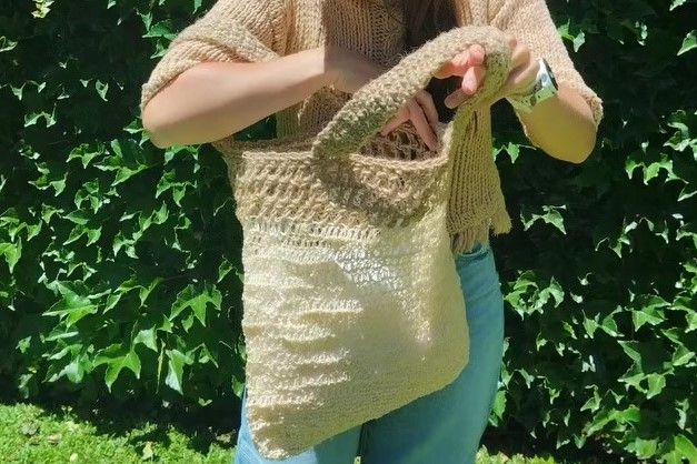 Primer plano de una mujer en un patio soleado sosteniendo el bolso modelo Arena de Nido Trama, resaltando la trama rústica y el diseño artesanal en tonos neutros.