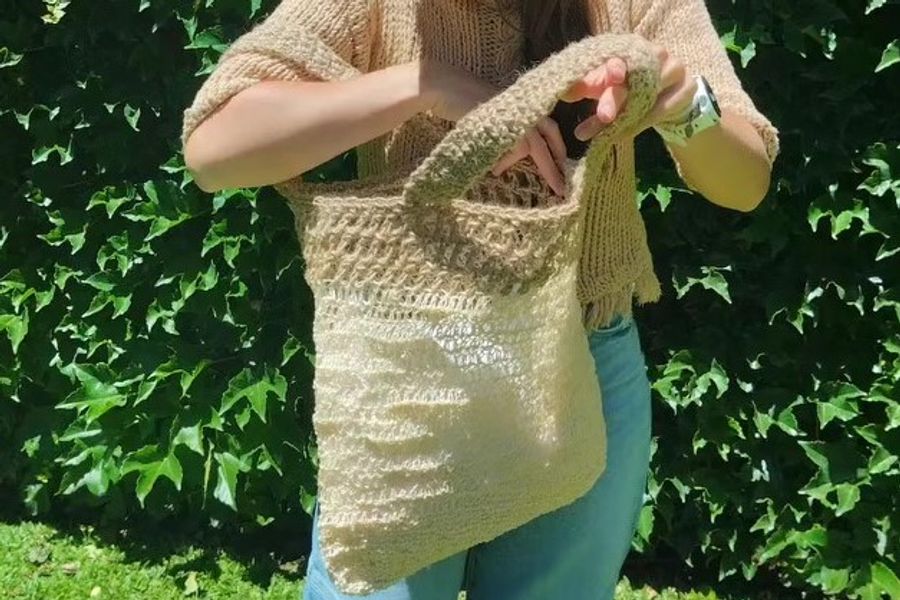 Primer plano de una mujer en un patio soleado sosteniendo el bolso modelo Arena de Nido Trama, resaltando la trama rústica y el diseño artesanal en tonos neutros.