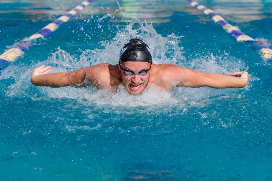 A swimmer surfaces from the pool while doing a breast stroke.