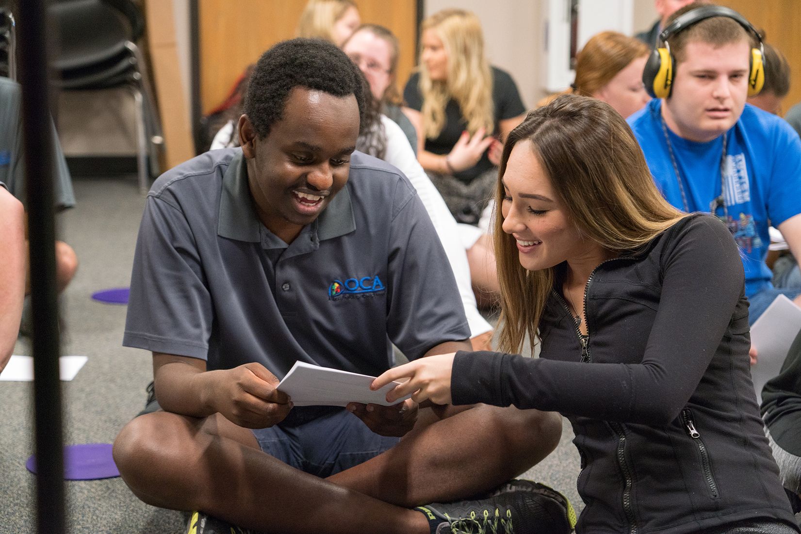 A college student and special needs student reviewing a paper while sitting on the floor.