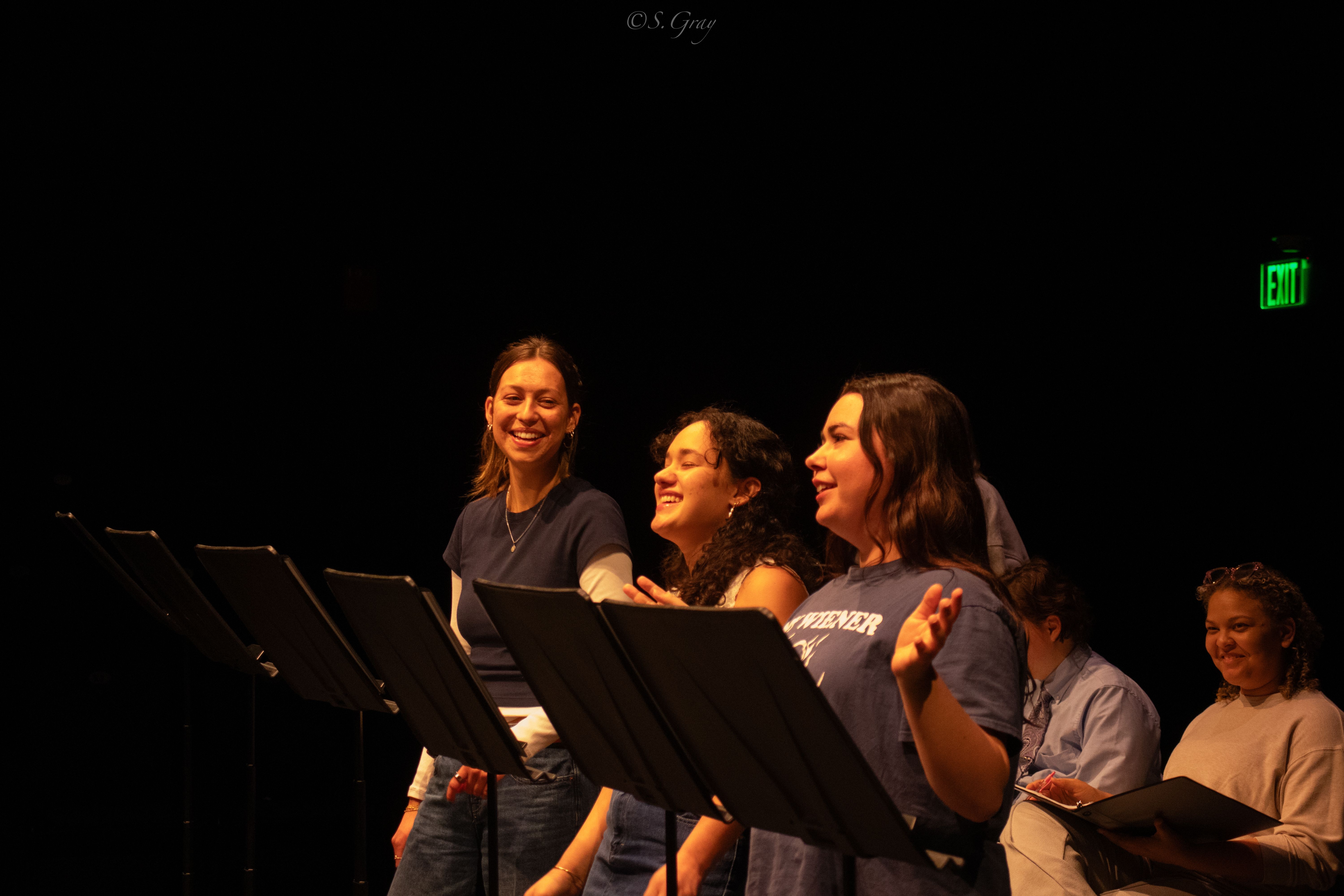 Performers reading scripts onstage, smiling.