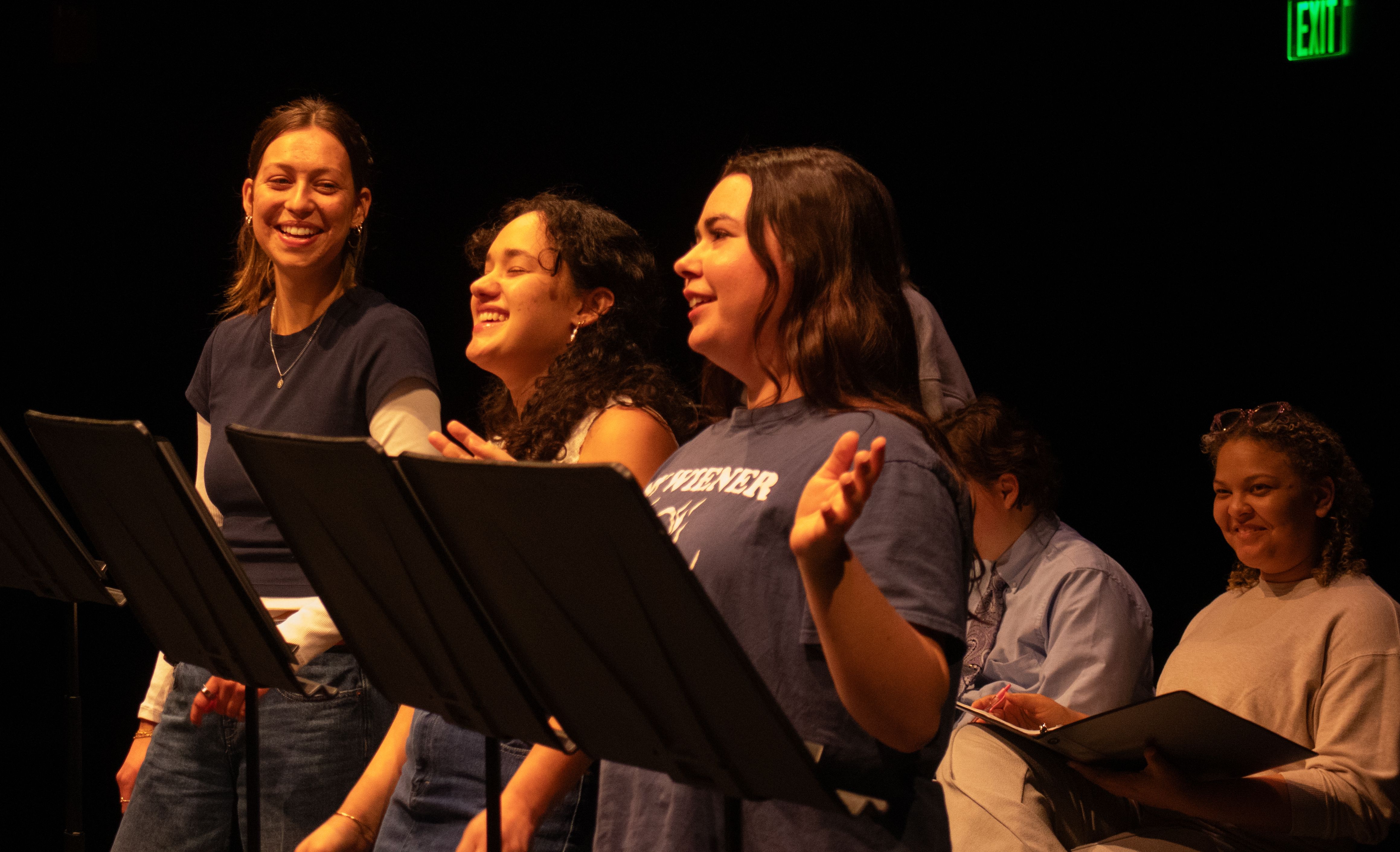 Performers reading scripts onstage, smiling.