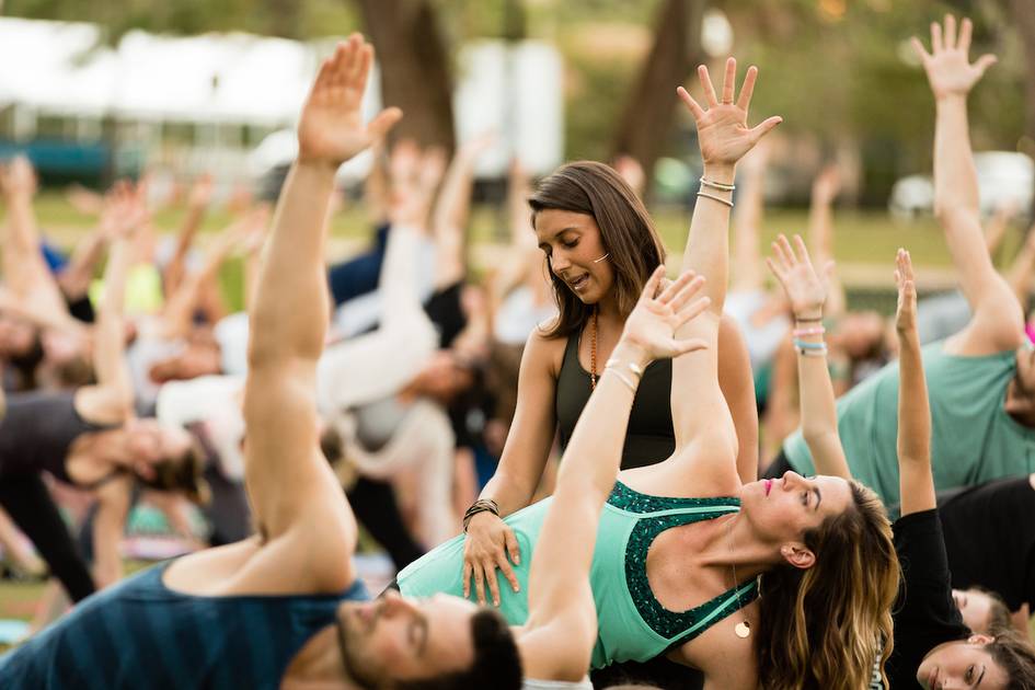 Instructor leads a large outdoor group yoga session.