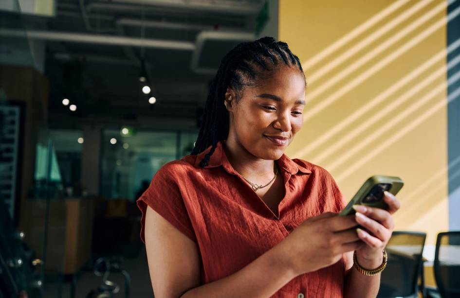 Person smiling while using a smartphone in a modern office space