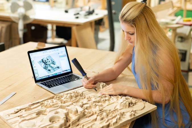 Student carving a wooden relief project on tabletop.