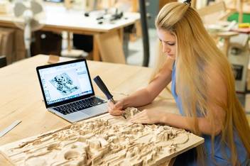 Student carving a wooden relief project on tabletop.