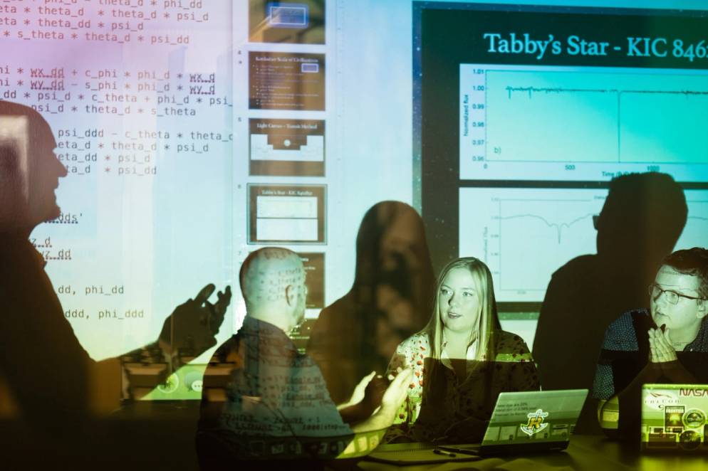 A professor and two students conduct physics research.