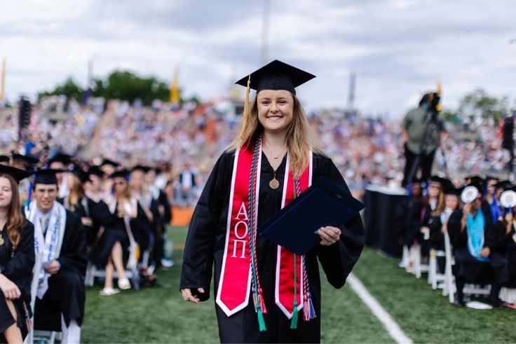 Rollins graduate in cap and gown holding diploma during outdoor commencement ceremony