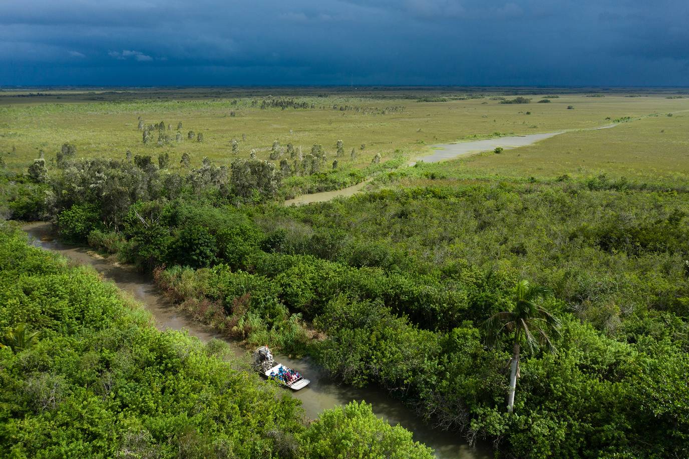 An aerial photo of an airboat driving through a canal with a storm on the horizon.