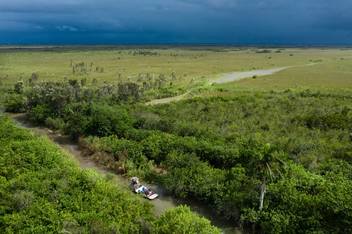 An aerial photo of an airboat driving through a canal with a storm on the horizon.