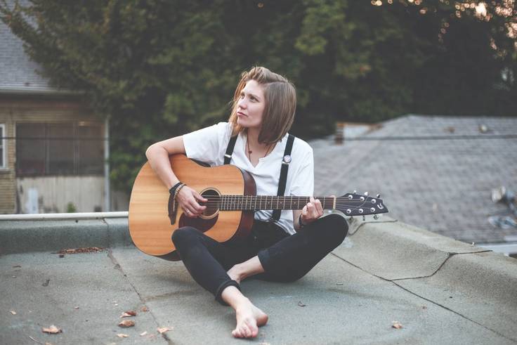 Grace Loescher playing a guitar on a rooftop.