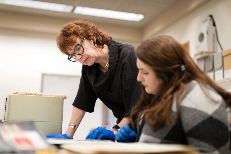 Claire Strom looking at research documents with a student while wearing protective gloves.